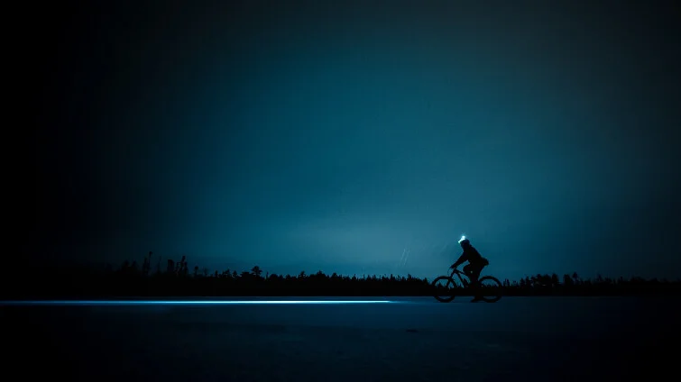 En man cyklar i mörkret med en pannlampa.