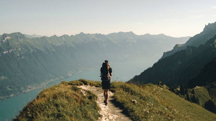 En man med vandringsskor vandrar längst en bergsstig med utsikt över en fjord.