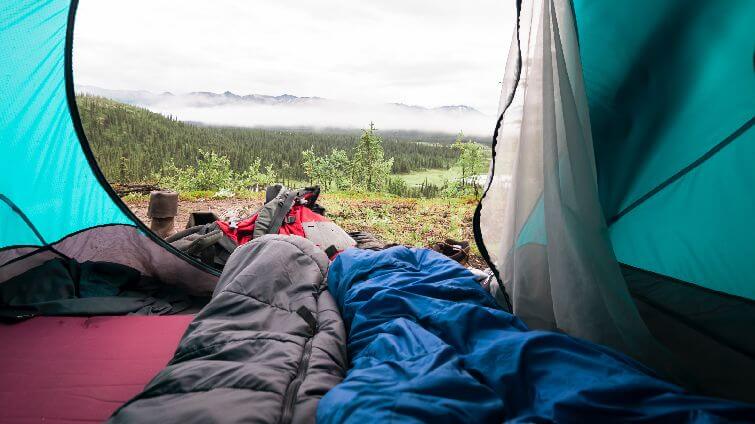 Två sovsäckar ligger i en tältöppning med en fin natur i bakgrunden.