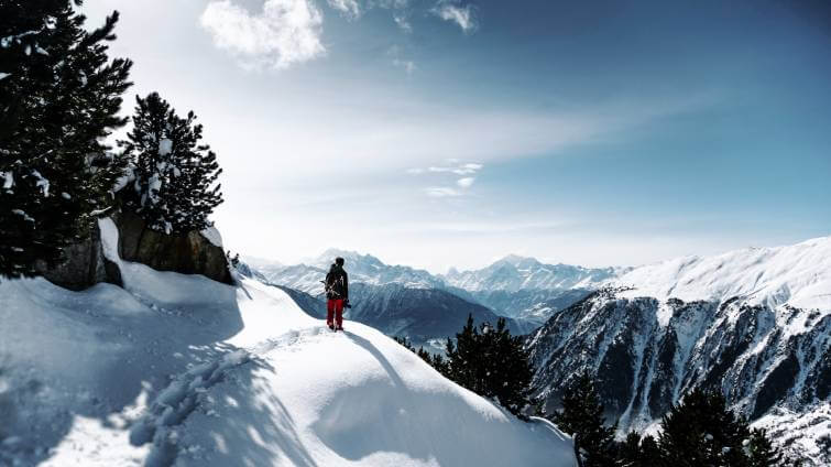 En dam med vinterkängor vandrar i ett snöigt bergslandskap.