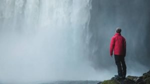 En man med regnbyxor och regnjacka tittar på ett vattenfall.