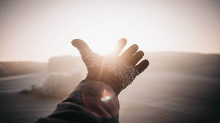 En person med vinterhandskar håller upp handen framför en soluppgång.