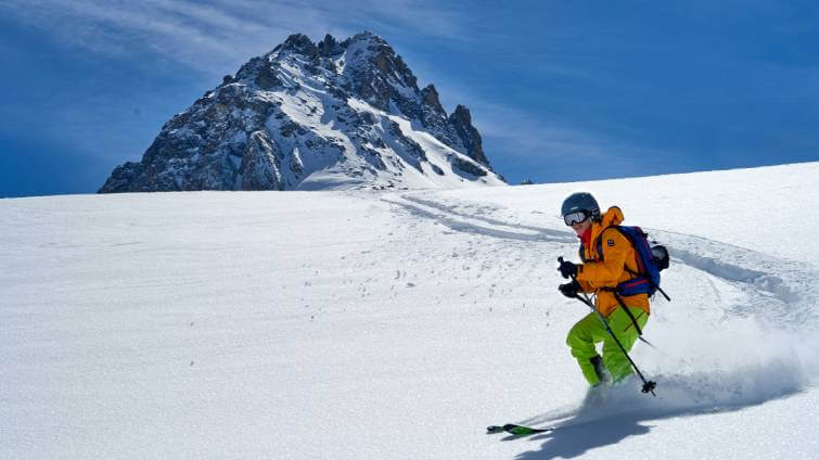 En skidåkare testar skidkläder på en tur nedför ett fjäll i pudersnö.