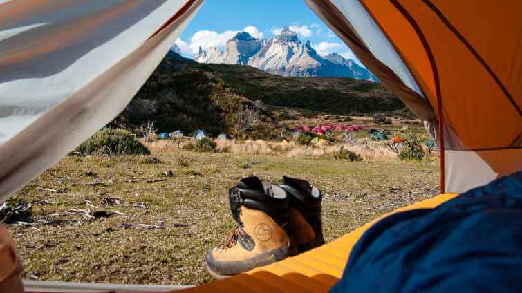 En person ligger på ett liggunderlag i ett tält och tittar på en vacker utsikt.